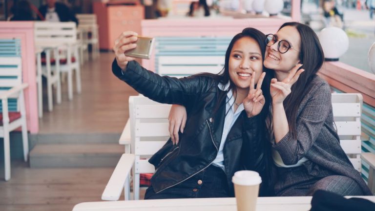 Two young women capturing a fun selfie moment in a stylish cafe setting.