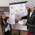 Navigating Hyper-Reality: Strategic Leadership for Digital Age Two young coworkers discuss a project using sketches and VR headset inside a cozy office.