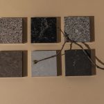 Artistic composition of square stone tiles with a twig on a neutral surface, showcasing minimalism.