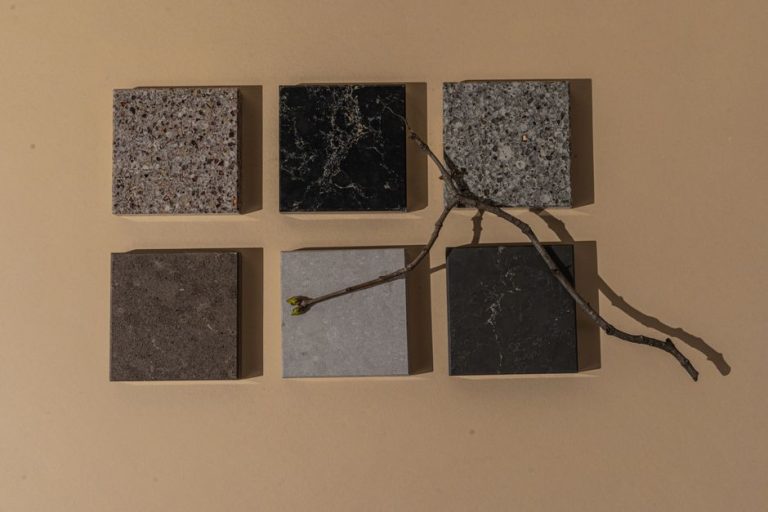 Artistic composition of square stone tiles with a twig on a neutral surface, showcasing minimalism.