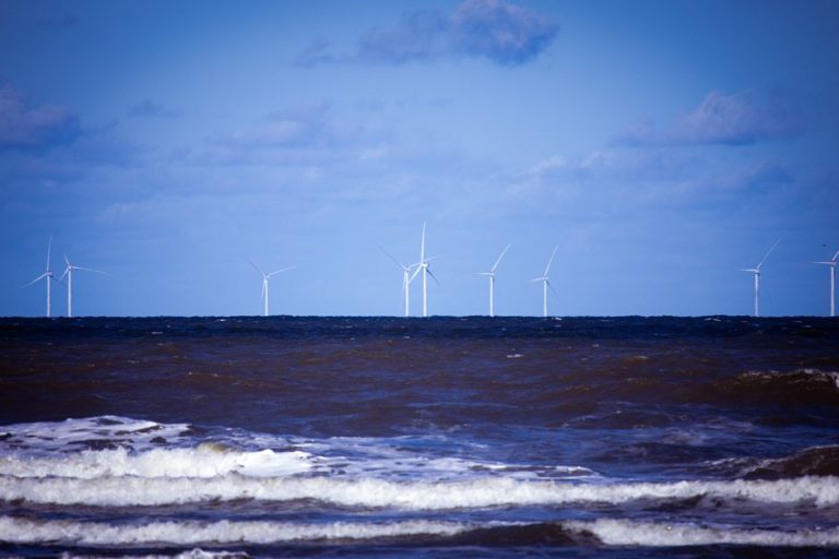 Offshore wind turbines generating sustainable energy over a calm ocean under a clear blue sky.