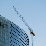 Contemporary glass building under construction with a visible crane against a clear blue sky.