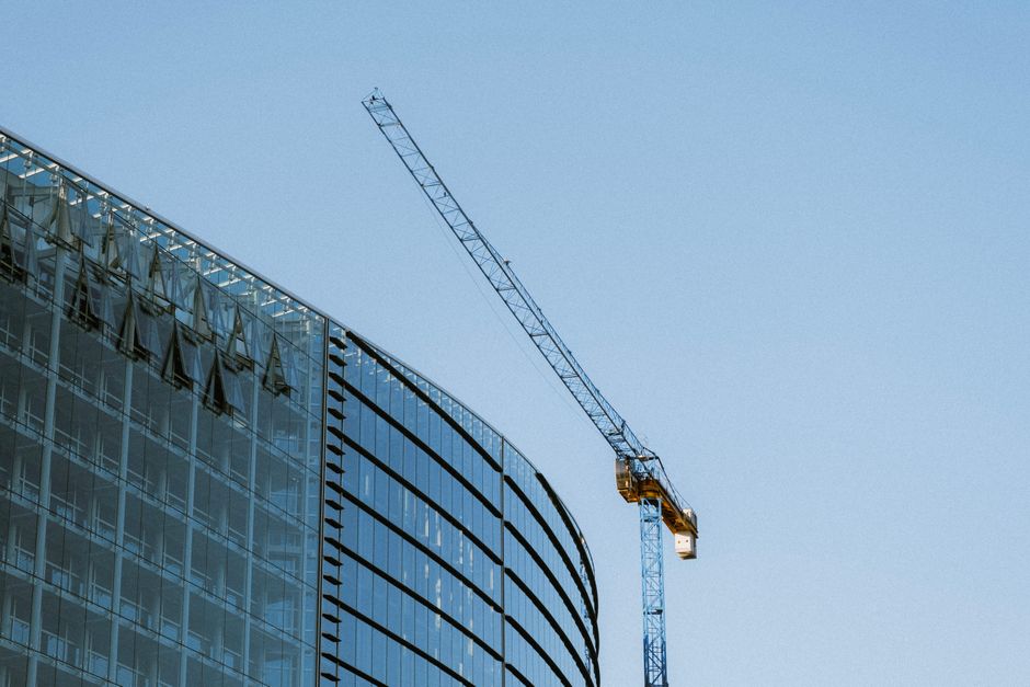 Contemporary glass building under construction with a visible crane against a clear blue sky.