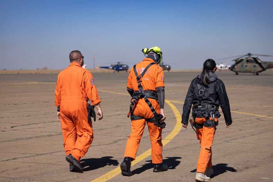 Rescue personnel in orange uniforms walking on airport tarmac with helicopters during the day.