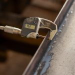 Close-up of digital caliper measuring the thickness of a metal object, showcasing precision engineering.
