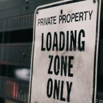Close-up of a private property loading zone only sign with urban backdrop.
