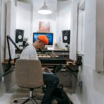 An adult male focuses on music production in a sleek, white recording studio setting.