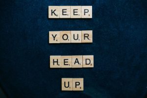 Inspirational message 'Keep Your Head Up' in Scrabble tiles on a dark blue background.
