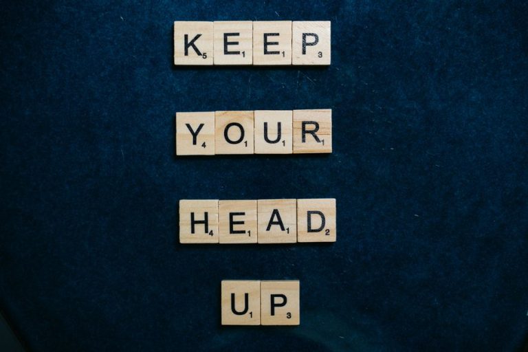 Inspirational message 'Keep Your Head Up' in Scrabble tiles on a dark blue background.
