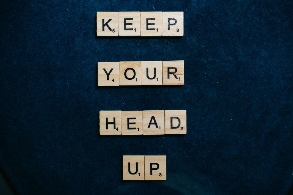 Inspirational message 'Keep Your Head Up' in Scrabble tiles on a dark blue background.
