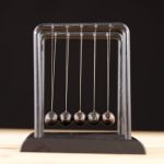 Close-up of a Newton's Cradle resting on a wooden surface against a dark background.