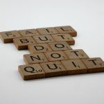 Wooden Scrabble tiles arranged to spell 'Fail but do not quit,' inspiring determination.