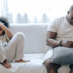 Overcoming Digital Alienation: Strategies for Modern Leadership Concentrated African American man in nightwear using smartphone while sitting on cozy sofa with son resting with joystick in light room