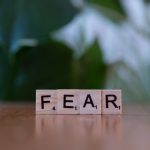 Overcoming Epistemological Insecurity in Strategic Decisions Wooden letter blocks spelling 'FEAR' on table against blurred green background. Emphasizes emotion and challenge.