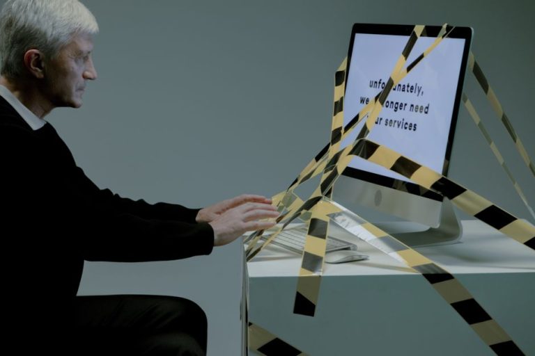 Elderly man at computer with termination notice, facing unemployment.