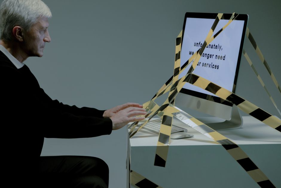 Elderly man at computer with termination notice, facing unemployment.