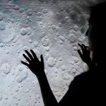 A mysterious silhouette of a woman interacting with a moon surface projection, evoking exploration and wonder.