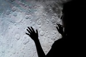 A mysterious silhouette of a woman interacting with a moon surface projection, evoking exploration and wonder.