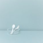 Plastic-Eating Enzymes: A New Paradigm for Circular Economy A minimalist still life featuring plastic cutlery in a container against a light blue background.