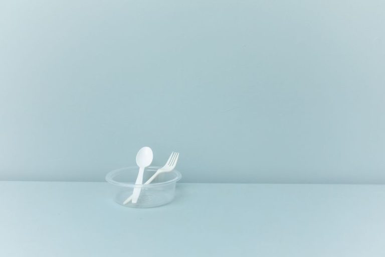 A minimalist still life featuring plastic cutlery in a container against a light blue background.
