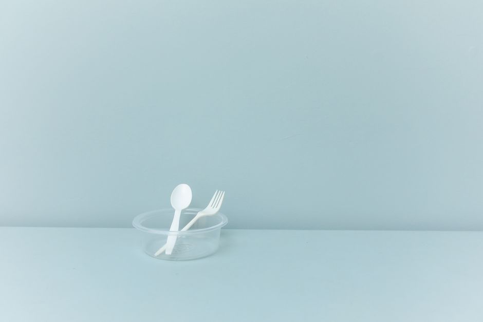 A minimalist still life featuring plastic cutlery in a container against a light blue background.