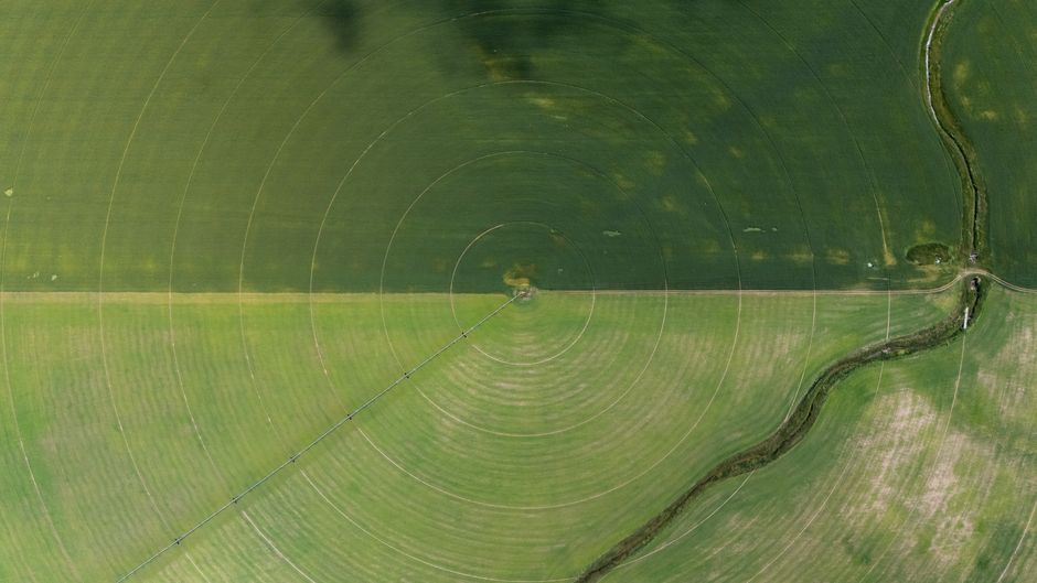 Aerial view showcasing farming irrigation circles and a river beside green fields.