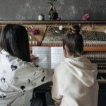 Back view of a piano lesson featuring a teacher guiding a student on music notation.