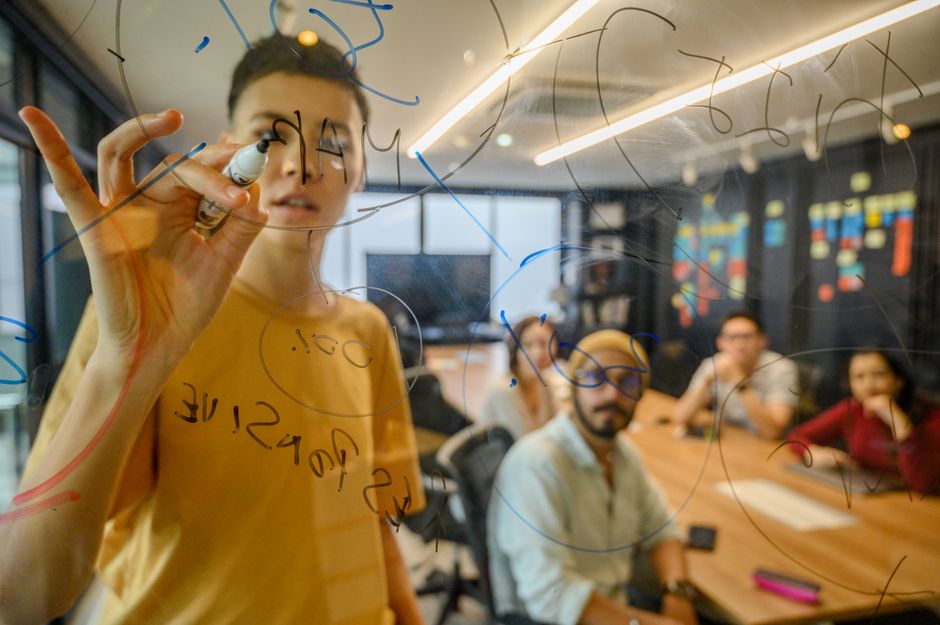 Team engaging in a collaborative meeting, brainstorming on a glass board in a modern office.