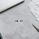 Reject Technological Determinism: Reclaim Your Strategic Agency Top view of scattered paper squares, laptop, and scissors forming the word 'NO', implying rejection or denial.