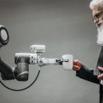 An elderly man receives a cup from a robotic arm in a modern office setting.