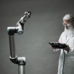 A scientist in a lab coat operates a high-tech robotic arm in a laboratory setting.