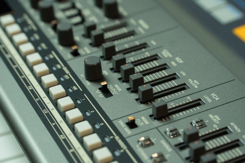 Detailed view of a music mixing console with various sliders and buttons in a studio setting.