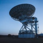 A large radio telescope under a clear evening sky captures cosmic signals.