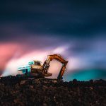 A dramatic excavator silhouette under vibrant northern lights and star trails captured at night.