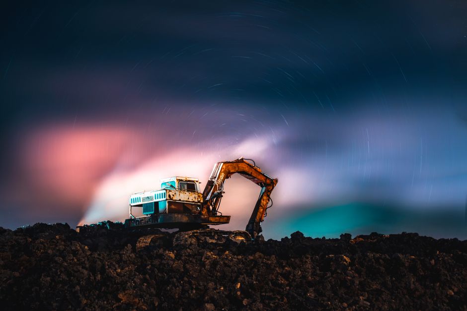 A dramatic excavator silhouette under vibrant northern lights and star trails captured at night.