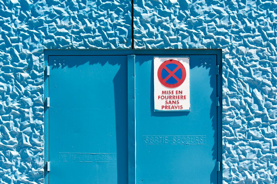 Bright blue textured wall with warning sign and exit door.