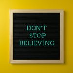 Inspirational message 'Don't Stop Believing' on a letter board against a vibrant yellow background.
