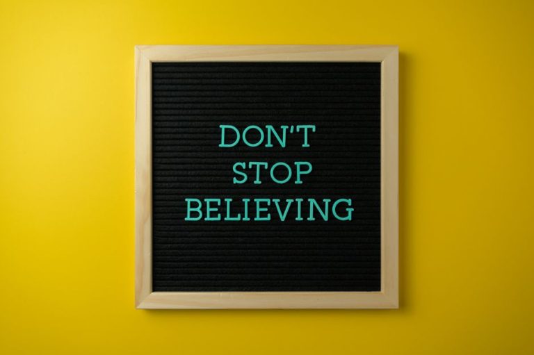 Inspirational message 'Don't Stop Believing' on a letter board against a vibrant yellow background.