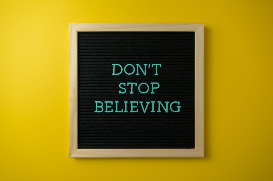 Inspirational message 'Don't Stop Believing' on a letter board against a vibrant yellow background.