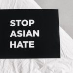 Black sign with 'Stop Asian Hate' on white fabric, promoting social justice.