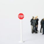 Stop Solving: Why Technical Leaders Need 'Strategic Boredom' to Fuel Innovation A miniature stop sign stands out with blurred figures in business attire, representing a conceptual business metaphor.