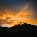 Three wind turbines silhouetted on a hill at sunset, showcasing renewable energy on a dramatic landscape.