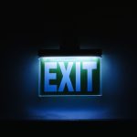 Strategic Exit: Why Knowing When to Quit is the Ultimate Executive Skill Photo of a glowing green exit sign in a dark environment, symbolizing safety and direction.