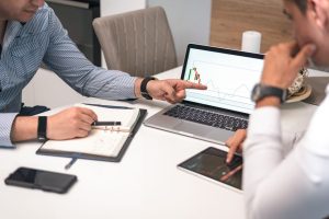 Two businessmen analyzing financial charts and data on a laptop and tablet.