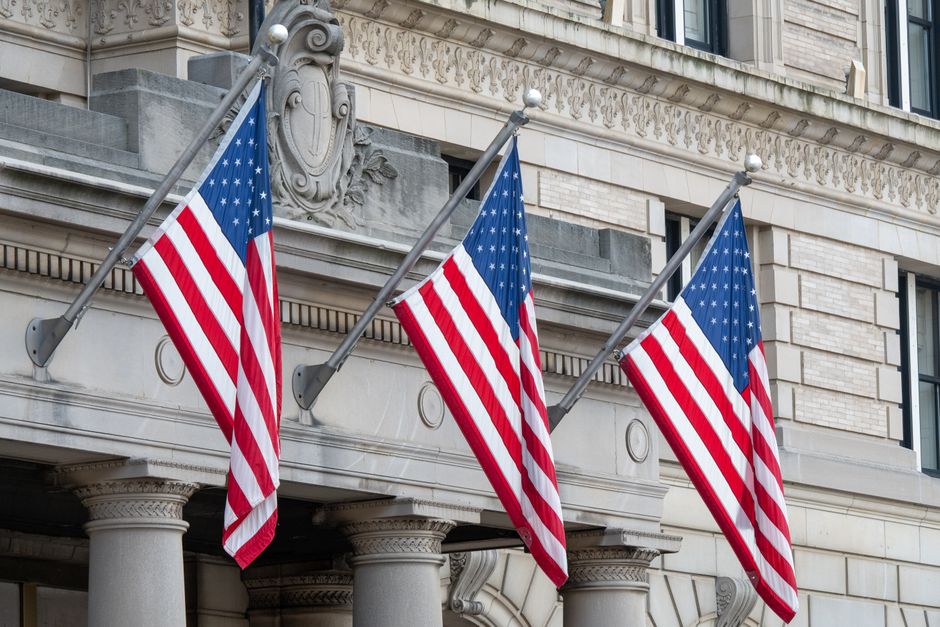 Three American flags hanging on a historic Boston building façade, symbolizing patriotism.