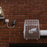 Close-up view of a brick wall featuring a LED light and a caged security camera.