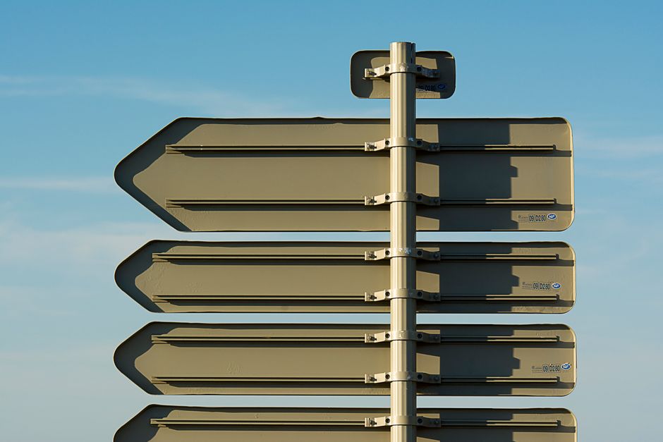 Back view of multiple blank directional signs against a blue sky.