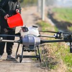 Person using a drone for agricultural purposes on a countryside pathway in Hefei, China.