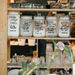 Collection of various glass jars with different dry food and glassware placed on wooden shelf