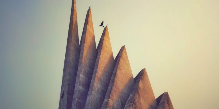 A bird flies over the National Martyrs' Memorial in Savar, highlighting its striking architectural form.